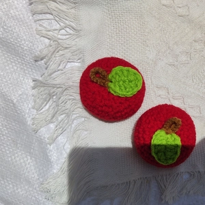 Close-up of handmade crochet apple charms with realistic yarn texture and green leaf