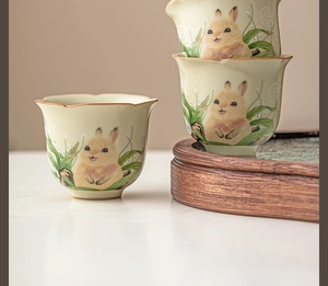 Detail of Ru Kiln ceramic tea cups with hand-painted rabbit motif on wooden tray