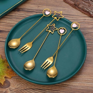 Golden 304 stainless steel cutlery set with heart and star pendants on green ceramic plate