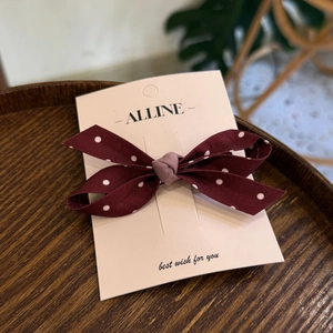 Detail of burgundy polka dot bow hair clip displayed on branded paper card over wood