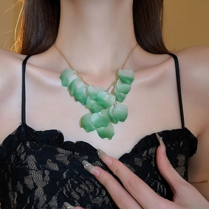 Detail of green gradient petal charms on a gold chain necklace worn on the collarbone