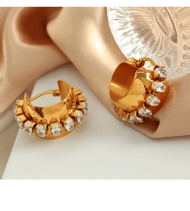 Macro shot of 18K gold plated C-shape earrings with oval cubic zirconia on satin fabric
