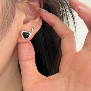 Close-up of black heart and silver star stud earrings worn on the earlobe