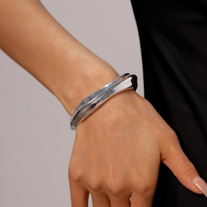 Close-up of a chunky silver metallic wavy cuff bracelet with mirror finish on a wrist