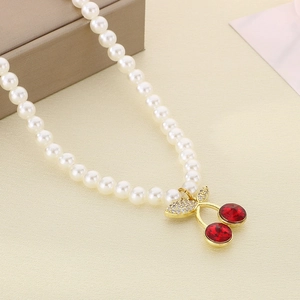 Detail of red cherry pendant with rhinestones on a pearl necklace with golden finish