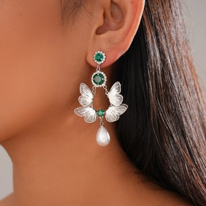 Detail of silver butterfly earrings with green stones, pearls and tassel on model