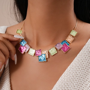 Detail of colorful geometric enamel squares on a gold chain necklace worn by a model