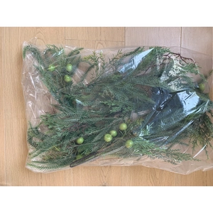 Close-up of artificial pine branches with green berries in clear plastic packaging