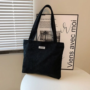 Detail of black corduroy tote bag with fashion label on indoor minimalist background