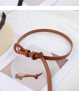 Detail of a brown slim leather belt featuring a stylish bow knot design on a magazine