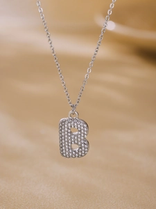 Macro view of silver letter B pendant with sparkling 5A zircon inlay on stainless steel necklace