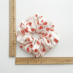 Macro view showing a large cream satin scrunchie with red lip prints measuring 12cm