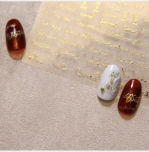 Macro detail of 3D embossed gold butterfly nail stickers with artistic lettering on nails