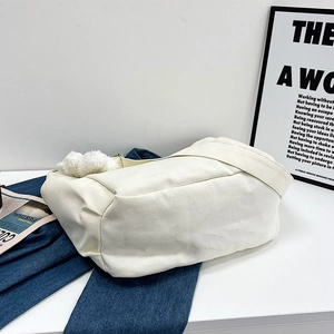 Minimalist white canvas tote bag with pompom charm on blue denim background
