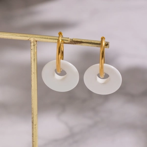 Classic gold stainless steel drop earrings with white natural stone donuts on a display stand