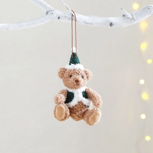 Plush Christmas teddy bear ornament with festive hat and vest hanging on a white branch