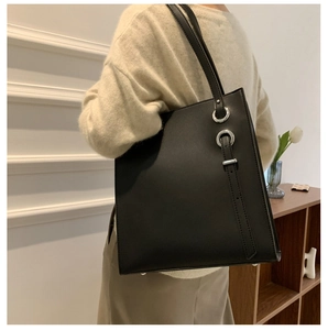 Model wearing a large black leather bucket bag featuring silver buckle and ring details
