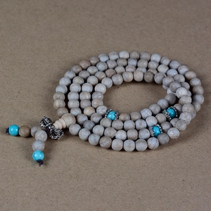 Natural camphor wood 108 prayer beads bracelet with turquoise accents on textured background
