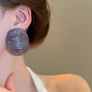 Close-up of oversized dark purple resin earrings with brushed texture on female model
