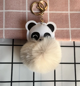 Close-up of a panda keychain with a beige faux fur ball and golden metal accessories