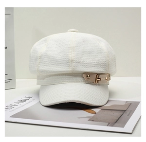 Close-up of cream textured newsboy hat with leather strap and engraved gold buckle