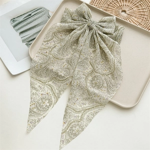 Detail of light green paisley bow hair clip with long ribbons on a beige tray
