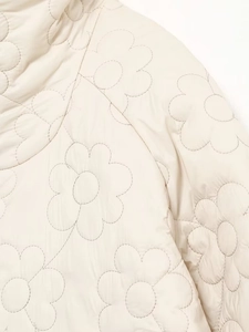 Macro detail of cream quilted jacket featuring intricate floral daisy stitching patterns