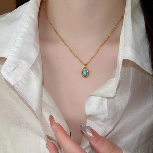 Close-up of a gold necklace with a vintage turquoise and zircon pendant on a model