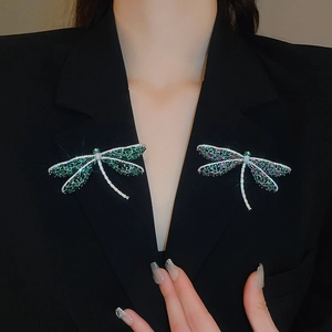 Detail van twee libelle broches met groene en paarse stenen op een zwart colbert revers