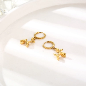 Close-up of golden balloon dog earrings on a white minimalist tiered display stand