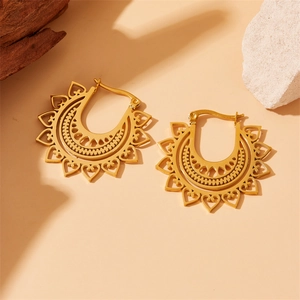 Macro detail of golden hollow heart earrings with geometric patterns on a wooden prop