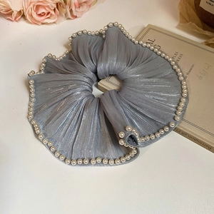 Detailed view of silver grey pleated fabric scrunchie with white pearl trim on vintage background