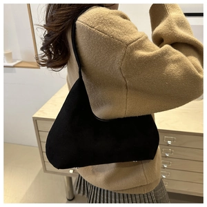 Detail shot of a black matte shoulder bag worn over a warm yellow sweater