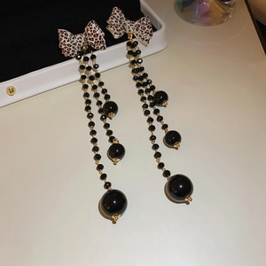 Detail view of leopard print bow earrings with long black beaded tassels and gold hardware