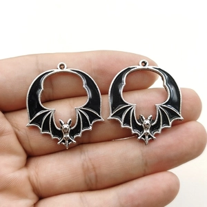 Gothic bat charms in hand showing size, black enamel with silver metal finish