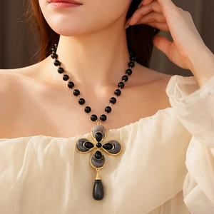 Close-up of vintage flower drop necklace with black marble clover pendant on model