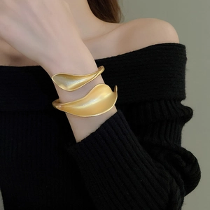 Macro shot of matte gold cuff bracelet featuring a sculptural floral leaf wrap design
