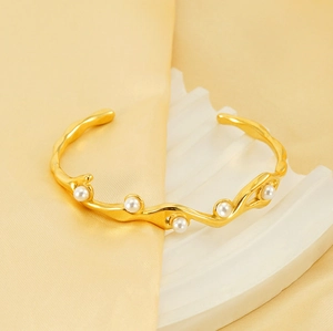 Dettaglio del bracciale a onde placcato oro 18k con perle bianche su sfondo di seta