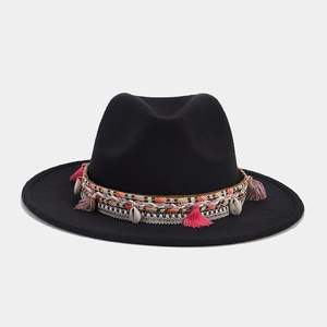 Détail d'un chapeau fedora noir avec ruban tissé, pompons roses et décorations en coquillages