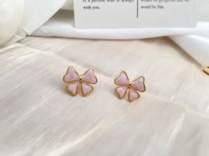 Macro detail of pink bow earrings with golden frame on pearlescent fabric background