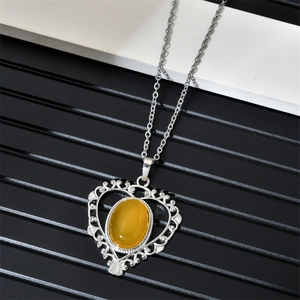 Détail du collier argenté en forme de cœur avec une pierre jaune sur marbre