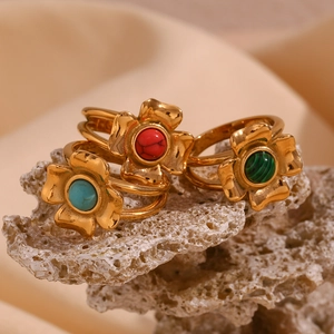Macro view of gold flower rings with malachite, turquoise and red stone on coral stone