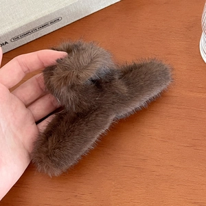 Gros plan d'une grande pince à cheveux en fausse fourrure marron foncé sur bois