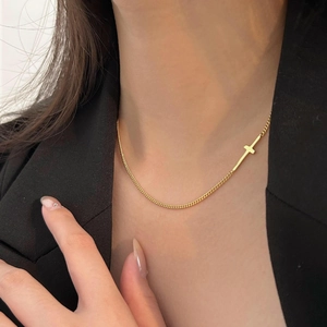 Detail of a minimalist gold cross pendant on a fine choker chain worn by a model