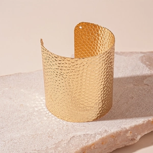 Detailed view of wide gold open cuff bracelet with textured hammered metal pattern