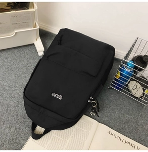 Flat lay of minimalist black backpack with books and water bottle on grey carpet
