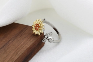 Detail of silver bee and golden sunflower ring with orange zircon inlays on wood