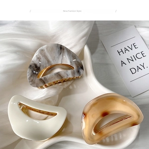 Three acetate hair claws in marble gray, cream white, and amber on white satin