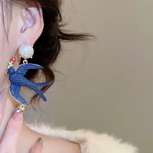 Detail of gold swallow earring with blue enamel and white pearl on model's ear