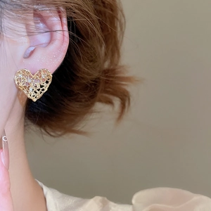 Detailed close-up of golden hollow heart earrings with lace texture and cubic zirconia
